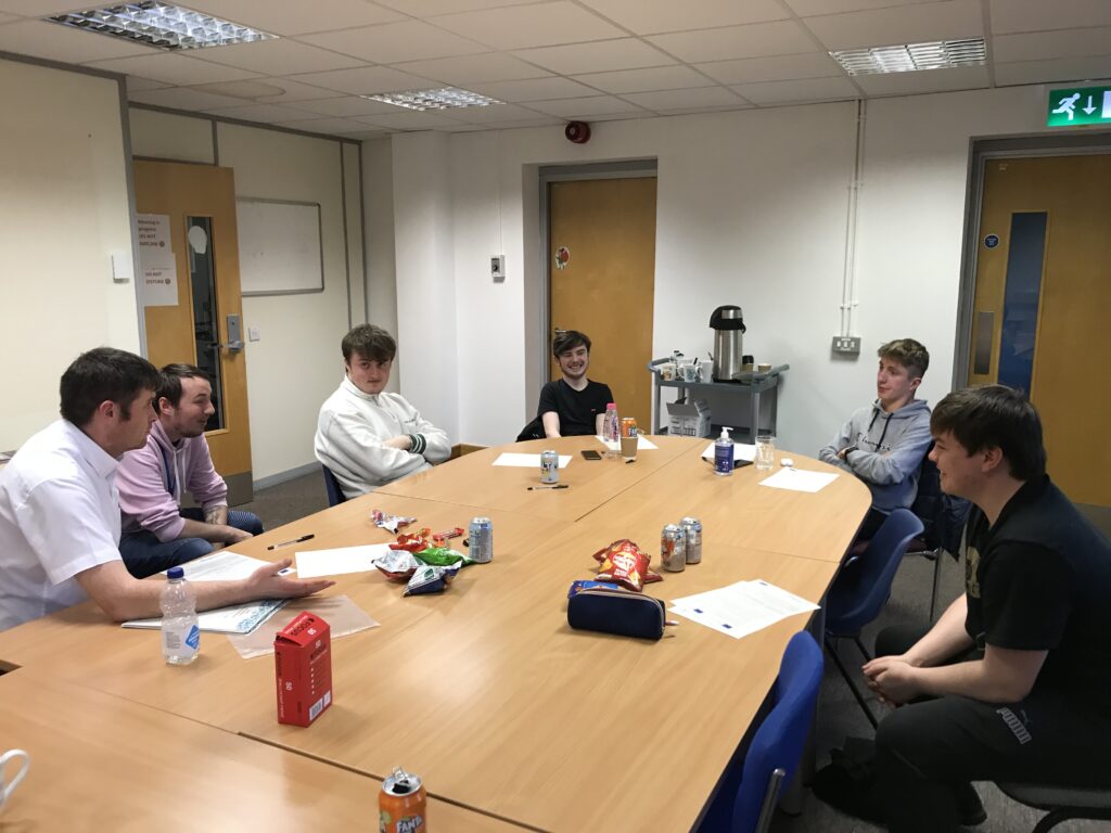 A group of young people sitting around a desk talking with David Curry (Young People's Engagement Worker). Cans of pop and crisps are in the middle of the table.