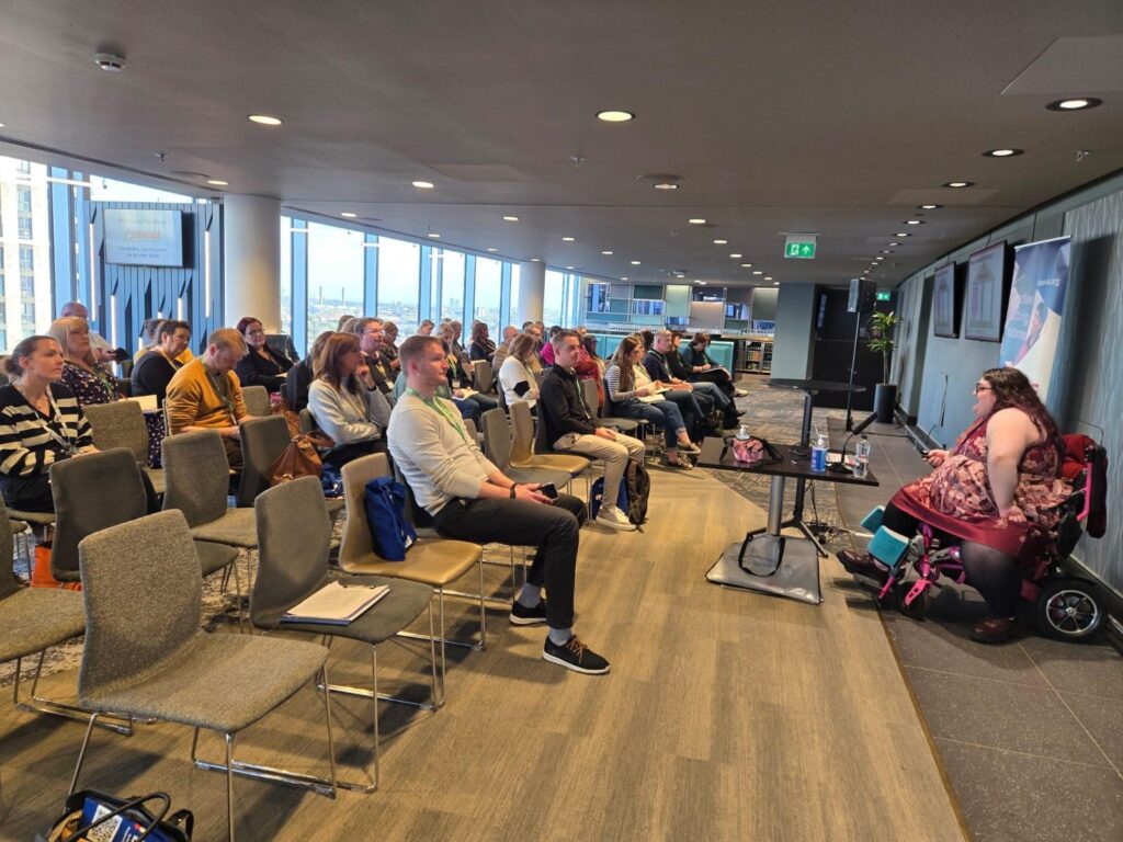 Megan Welton delivers a presentation to a group of people in a large open room.