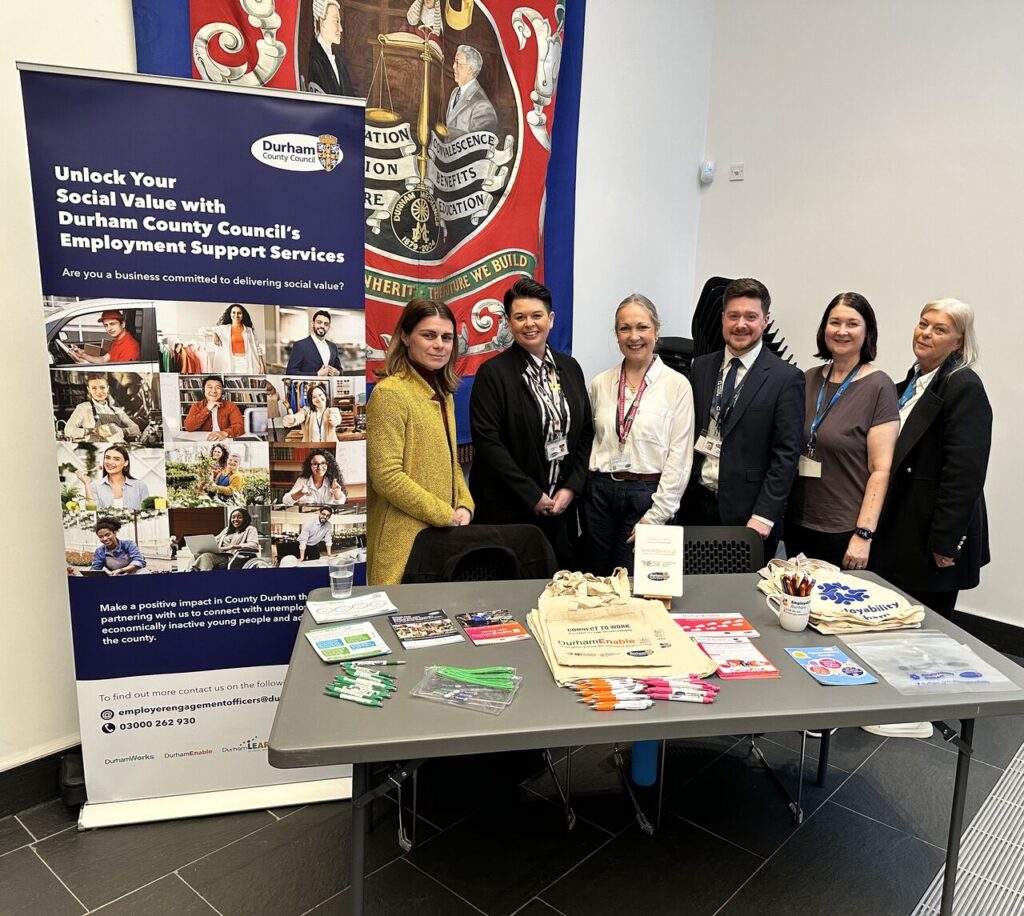 The Employer Engagement Team and Employability Durham staff pose new to a new banner behind a table of merch.