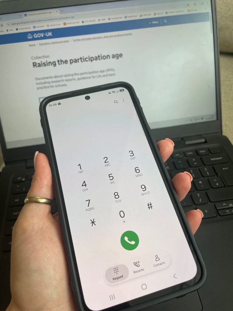 Hand holding mobile phone in from of laptop